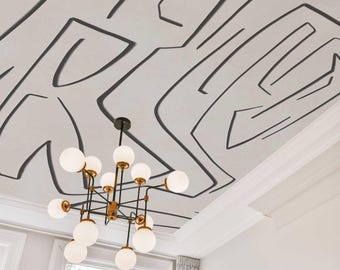 May include: A contemporary chandelier with spherical white lights suspended from a white ceiling featuring a black abstract pattern. The chandelier has a black and gold frame. A window with white trim and curtains is visible.