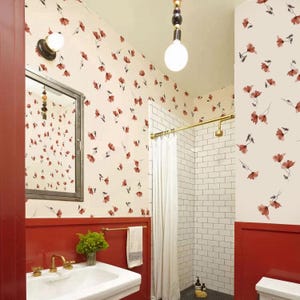May include: A bathroom featuring red and cream floral wallpaper. The lower walls are painted red, with a white tiled shower. A white sink with gold taps and a mirror are also visible.