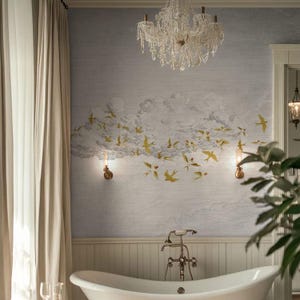 May include: A bathroom scene featuring a white clawfoot tub, a crystal chandelier, and a wall mural with a cloud and bird design. The mural has gold-colored birds and a light blue background. Two sconces flank the mural.