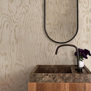 May include: A bathroom vanity featuring a square dark brown stone sink with a matching dark metal faucet, set atop a light wood cabinet. Above the sink is an oval mirror with a thin dark frame, positioned against a light wood grain wall.