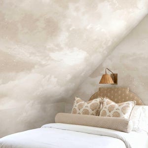 Peut inclure: Une chambre avec un papier peint au motif de ciel nuageux beige et blanc. Le lit comprend une couette blanche, un traversin cylindrique beige et deux oreillers carrés à motif de coquillages beiges. Une applique murale a un abat-jour en osier.