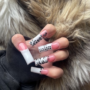 Puede incluir: Una mano con uñas acrílicas largas y cuadradas. Las uñas presentan varios diseños, incluyendo un estampado de leopardo blanco y negro, lunares negros y un patrón de cebra. Algunas uñas tienen una base rosa con una punta blanca.