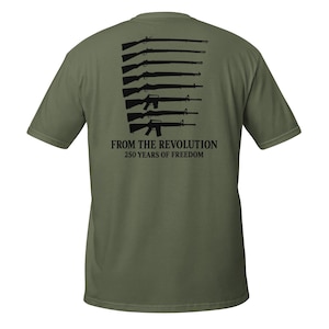 May include: Olive green t-shirt featuring a black graphic of various rifles and the text "FROM THE REVOLUTION 250 YEARS OF FREEDOM". The shirt has short sleeves and a crew neck.