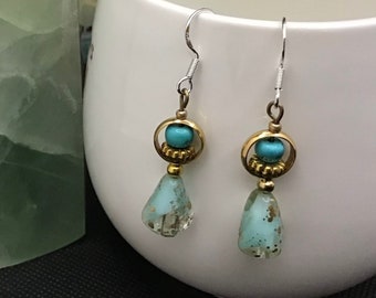 May include: A pair of turquoise and gold dangle earrings with a teardrop-shaped turquoise stone and a gold bead accent. The earrings are hanging from silver hooks.