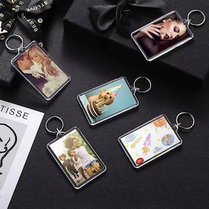 May include: A collection of clear acrylic keychains with various images. One keychain features a couple, another a dog with a birthday cake, and others with a woman, children, and a drawing of a rocket and planets. Each keychain has a silver ring.