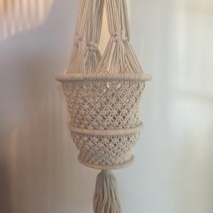 Peut inclure: Suspension pour plante en macramé crème, avec un design de panier tissé et une gland. Le porte-plante est suspendu par quatre cordons noués, parfait pour exposer de petites plantes en pot. La couleur neutre complète divers styles de décoration.