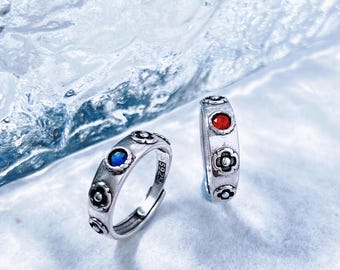 May include: Two silver rings with floral designs and colorful accents. One ring features a blue gemstone, while the other has a red gemstone. The rings have a vintage style and are set against a light blue background.