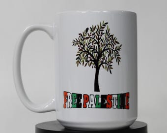 May include: White ceramic mug with a tree design in green and brown, and the text "FREE PALESTINE" in a colourful font. The mug has a large handle and is suitable for hot or cold drinks. The mug is a standard size.