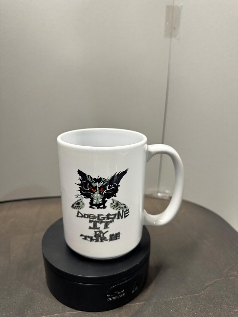 May include: White ceramic mug with a black and red graphic of a creature and the text "Dog Gone It By The Tree". The mug has a curved handle and is on a black rotating stand.