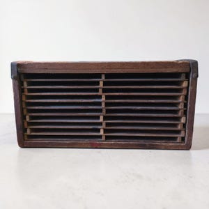May include: A rectangular wooden storage rack featuring multiple horizontal shelves arranged in a grid pattern. The structure is constructed from dark brown wood with thin wooden dividers and metal brackets secured at the top corners on both sides.