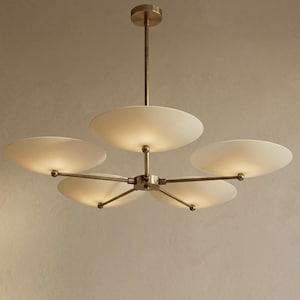 May include: A modern chandelier with five frosted glass shades. The light fixture has a brass finish and a central hub with radiating arms. Each shade is illuminated, casting a warm glow.