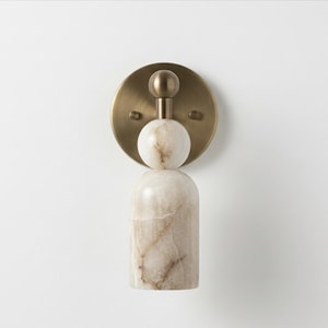 May include: A wall sconce featuring a circular brushed brass backplate with a central vertical arrangement of a small brass sphere, a white marble sphere, and a larger cylindrical white marble base with brown veining throughout the stone.