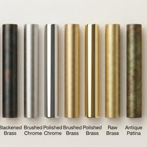 May include: A collection of cylindrical metal hardware samples in various finishes, including matte black, antique black, blackened brass, brushed chrome, polished chrome, brushed brass, polished brass, raw brass, antique patina, satin brass, and aged brass. Each sample is labeled with its finish name.