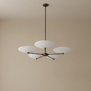May include: A modern chandelier with five white, disc-shaped shades. The fixture has a dark bronze finish and is suspended from a single rod. The shades are evenly spaced around a central hub, creating a balanced and elegant design.