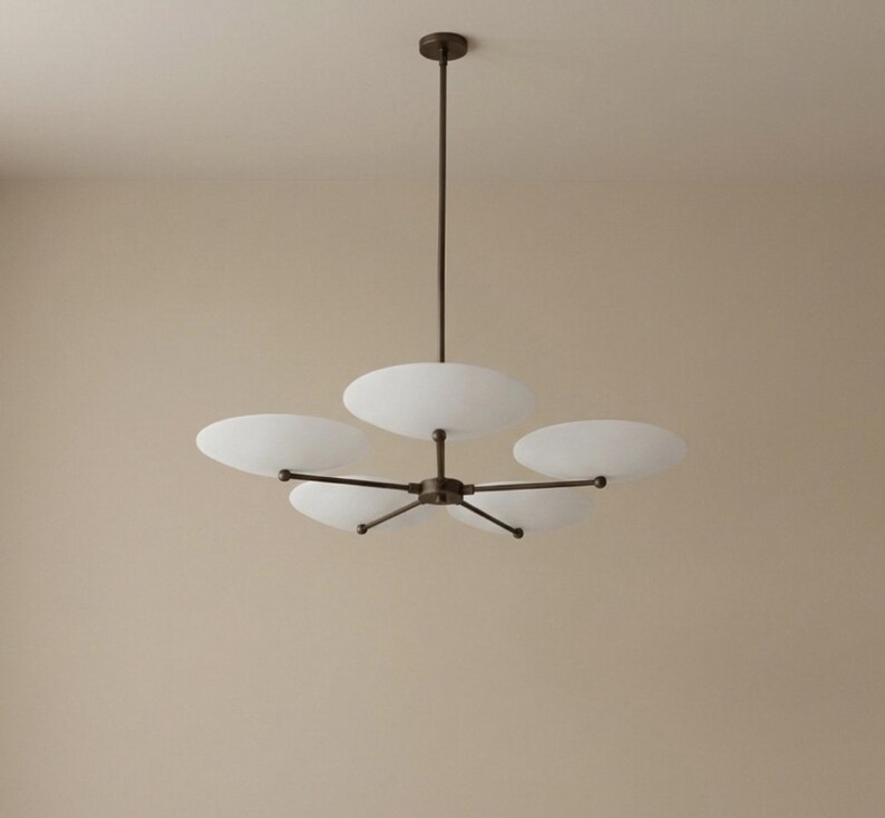 May include: A modern chandelier with five white, disc-shaped shades. The fixture has a dark bronze finish and is suspended from a single rod. The shades are evenly spaced around a central hub, creating a balanced and elegant design.