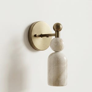 May include: A wall-mounted light fixture featuring a circular brushed brass backplate and a horizontal arm. The fixture includes a spherical brass finial atop a stacked design consisting of a white marble sphere and a cylindrical white marble base.