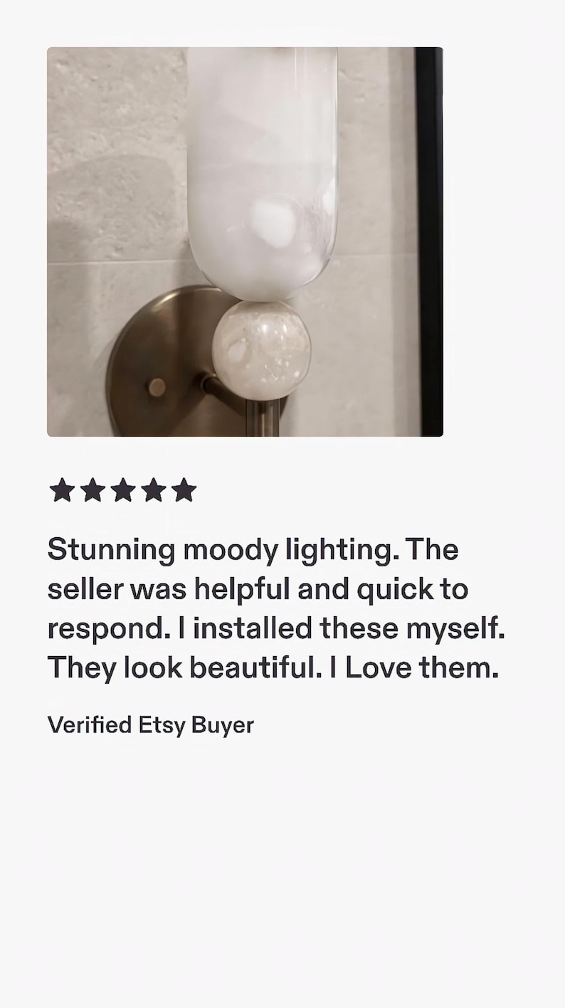 May include: A wall-mounted light fixture featuring a circular bronze-toned metal base and a vertical cylindrical glass shade. A small, spherical, textured white glass orb sits between the base and the main cylindrical glass light component.