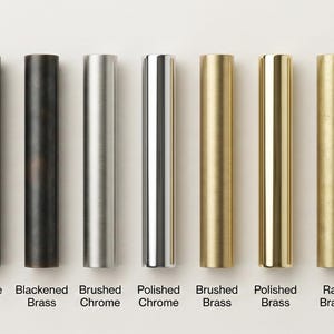 May include: Nine cylindrical metal hardware samples arranged in a row, featuring various finishes labeled as Matte Black, Antique Black, Blackened Brass, Brushed Chrome, Polished Chrome, Brushed Brass, Polished Brass, Raw Brass, and Antique Patina.
