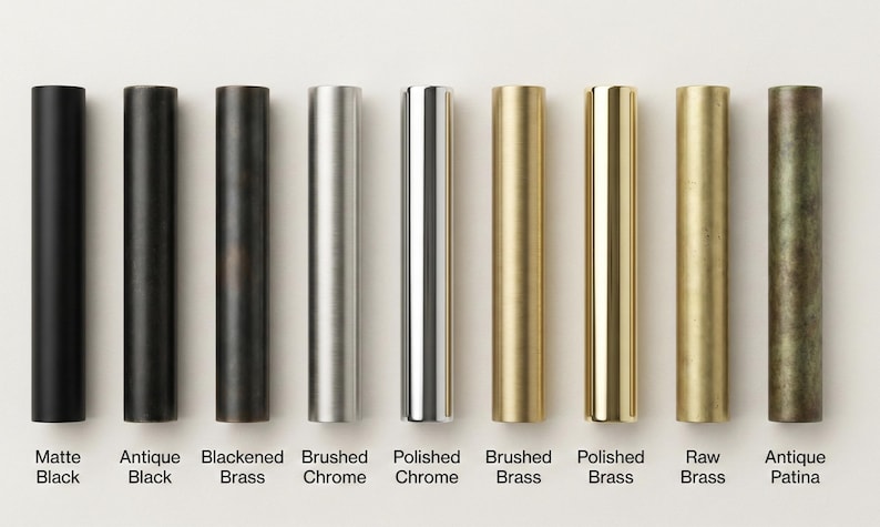 May include: Nine cylindrical metal hardware samples arranged in a row, featuring various finishes labeled as Matte Black, Antique Black, Blackened Brass, Brushed Chrome, Polished Chrome, Brushed Brass, Polished Brass, Raw Brass, and Antique Patina.