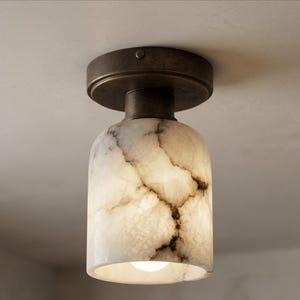 May include: A ceiling-mounted light fixture with a cylindrical, off-white shade featuring brown veining. The fixture has a dark bronze-colored base and a round top. The light bulb is visible at the bottom of the shade.