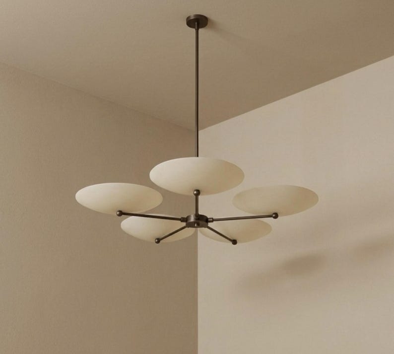 May include: A modern, five-light chandelier with a dark bronze finish. The fixture features five off-white, saucer-shaped shades extending from a central hub. The chandelier is suspended from the ceiling by a single rod.