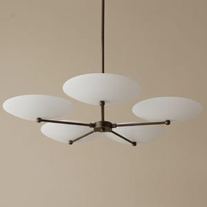 May include: A modern chandelier with five white, oval-shaped glass shades. The shades are attached to a dark bronze-colored metal frame. The fixture hangs from a single rod.