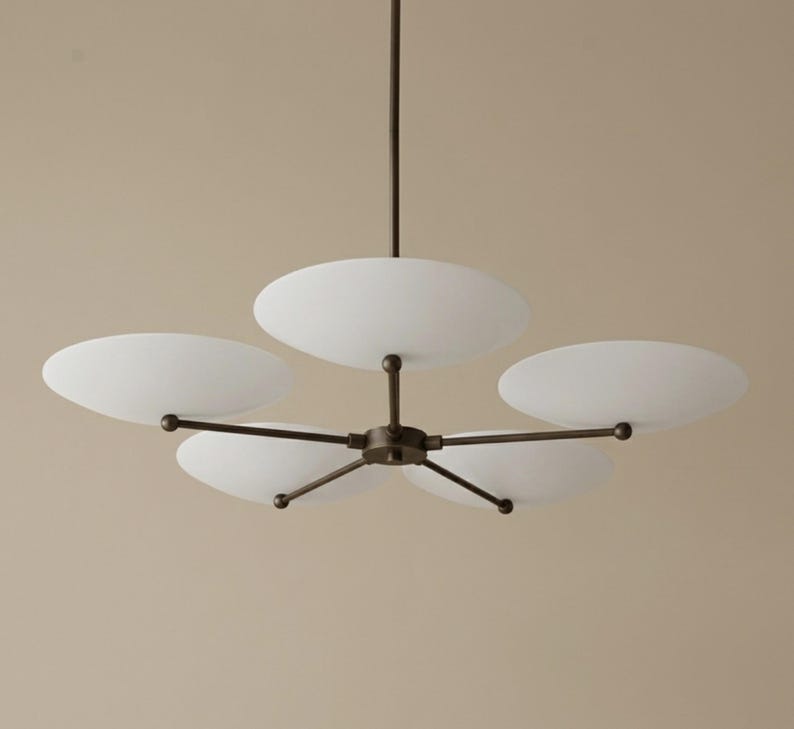 May include: A modern chandelier with five white, oval-shaped glass shades. The shades are attached to a dark bronze-colored metal frame. The fixture hangs from a single rod.