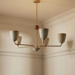 May include: A modern chandelier with five light fixtures. The light fixtures are a light beige color and are attached to gold-colored arms. The central stem is gold with a wooden sphere and a gold ceiling mount.
