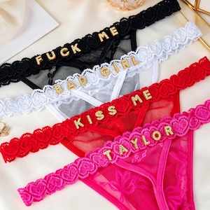 Puede incluir: Cuatro tangas de encaje en negro, blanco, rojo y rosa. Cada uno presenta texto de pedrería dorada: "FUCK ME", "BAD GIRL", "KISS ME" y "TAYLOR". El ribete de encaje tiene bordes festoneados.