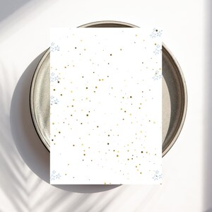 May include: A white card with a gold and blue star pattern rests on a gray plate. The stars are scattered across the card, with clusters of blue stars in the corners. The plate has a dark rim and a light gray center.