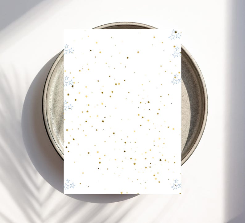 May include: A white card with a gold and blue star pattern rests on a gray plate. The stars are scattered across the card, with clusters of blue stars in the corners. The plate has a dark rim and a light gray center.