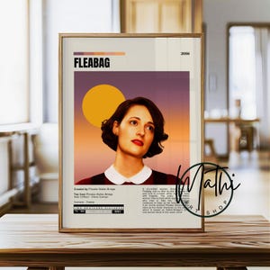 May include: A framed poster featuring the title "FLEABAG" with a portrait of a woman against a sunset-colored background. The poster includes the year 2016 and credits. The poster is displayed on a wooden surface.