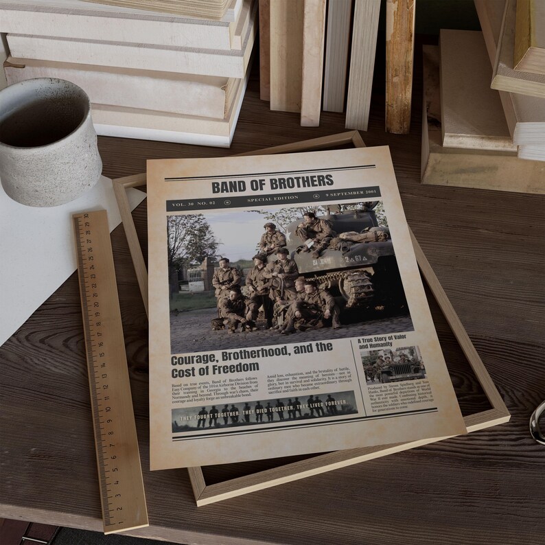 Pode incluir: Uma impress&atilde;o de jornal em estilo vintage intitulada "Band of Brothers" com uma fotografia de soldados em um tanque. A manchete diz "Courage, Brotherhood, and the Cost of Freedom". A impress&atilde;o &eacute; exibida em uma moldura de madeira.