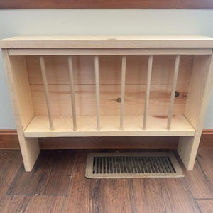 May include: A wooden hay feeder with a rectangular design. The feeder has a slatted front with vertical dowels and a solid top and base. The wood has a natural, light color.