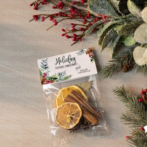 May include: A clear plastic bag filled with dried orange slices, cinnamon sticks, and other spices. The bag has a white tag attached to it that says "Holiday Potpourri Simmering Scent" from "Helen Griswold".