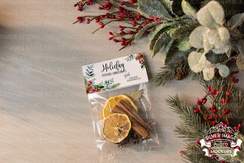 May include: A clear plastic bag filled with dried orange slices, cinnamon sticks, and other spices. The bag has a white tag attached to it that says "Holiday Potpourri Simmering Scent" from "Helen Griswold".