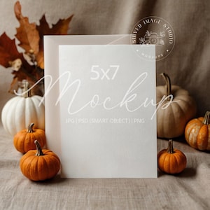 May include: A 5x7 mockup card with the word "Mockups" in a script font. The card is surrounded by small orange pumpkins, a white pumpkin, and fall foliage. The image has a neutral, autumnal theme.