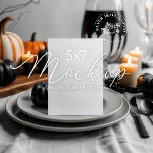 Könnte beinhalten: Ein 5x7 Mockup-Karte steht auf einem Teller, umgeben von Kürbissen, Kerzen und einem Weinglas. Die Szene hat ein Halloween-Thema mit schwarzen und orangefarbenen Kürbissen und brennenden Kerzen. Die Karte ist leer.