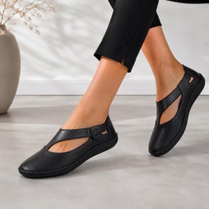 Puede incluir: Bailarinas de cuero negro con diseño de tira en T. Los zapatos tienen punta redondeada y cierre de hebilla lateral. Las suelas son negras y los zapatos parecen nuevos.