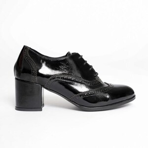 May include: A glossy black oxford shoe with a block heel. The shoe features decorative perforations along the seams and a lace-up closure. The heel measures approximately 2.5 inches.