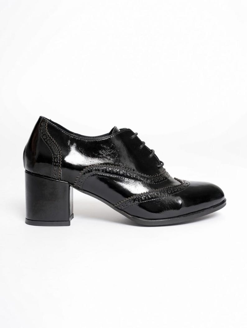 May include: A glossy black oxford shoe with a block heel. The shoe features decorative perforations along the seams and a lace-up closure. The heel measures approximately 2.5 inches.