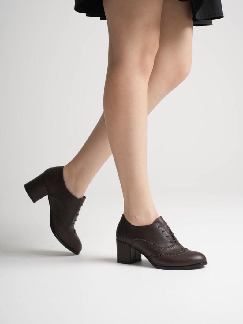 May include: Brown leather oxford-style shoes with a block heel. The shoes feature a lace-up design and decorative perforations along the seams. The heel height is approximately 3 inches.