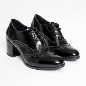 May include: A pair of black patent leather Oxford shoes with a block heel. The shoes have a classic lace-up design and decorative brogue detailing along the edges. The heels measure approximately 2.5 inches.