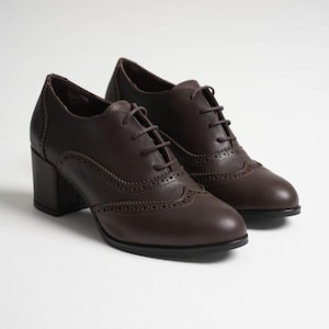 May include: A pair of brown leather oxford shoes with a block heel. The shoes have a classic brogue design with decorative perforations and lace-up closures. The heels are approximately 2.5 inches high.