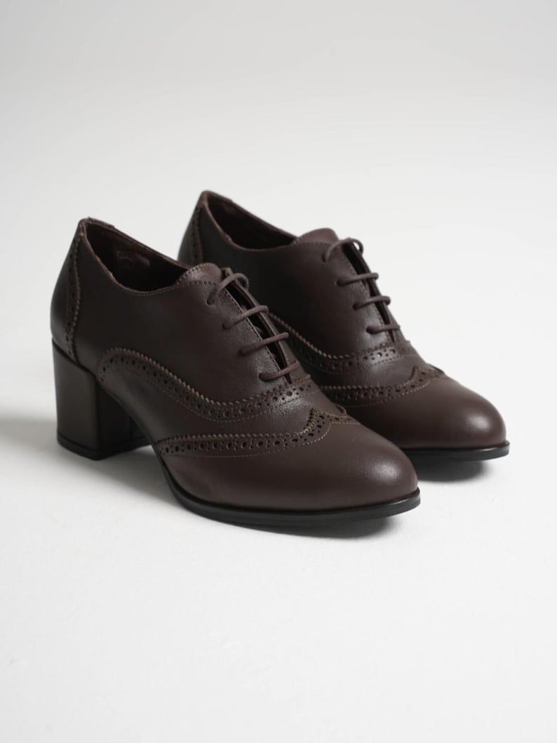 May include: A pair of brown leather oxford shoes with a block heel. The shoes have a classic brogue design with decorative perforations and lace-up closures. The heels are approximately 2.5 inches high.