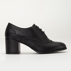 May include: Black leather oxford shoe with a block heel. The shoe features decorative perforations along the seams and a lace-up closure. The heel measures approximately 2.5 inches.