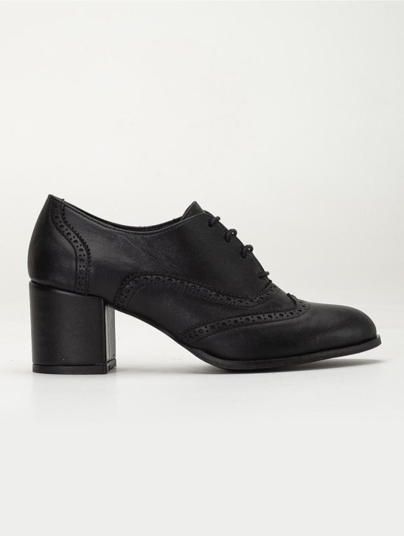 May include: Black leather oxford shoe with a block heel. The shoe features decorative perforations along the seams and a lace-up closure. The heel measures approximately 2.5 inches.