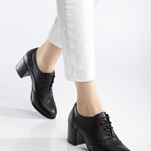May include: Black leather oxford-style shoes with a block heel. The shoes feature a lace-up design and decorative perforations along the edges. The heel height is approximately 3 inches.