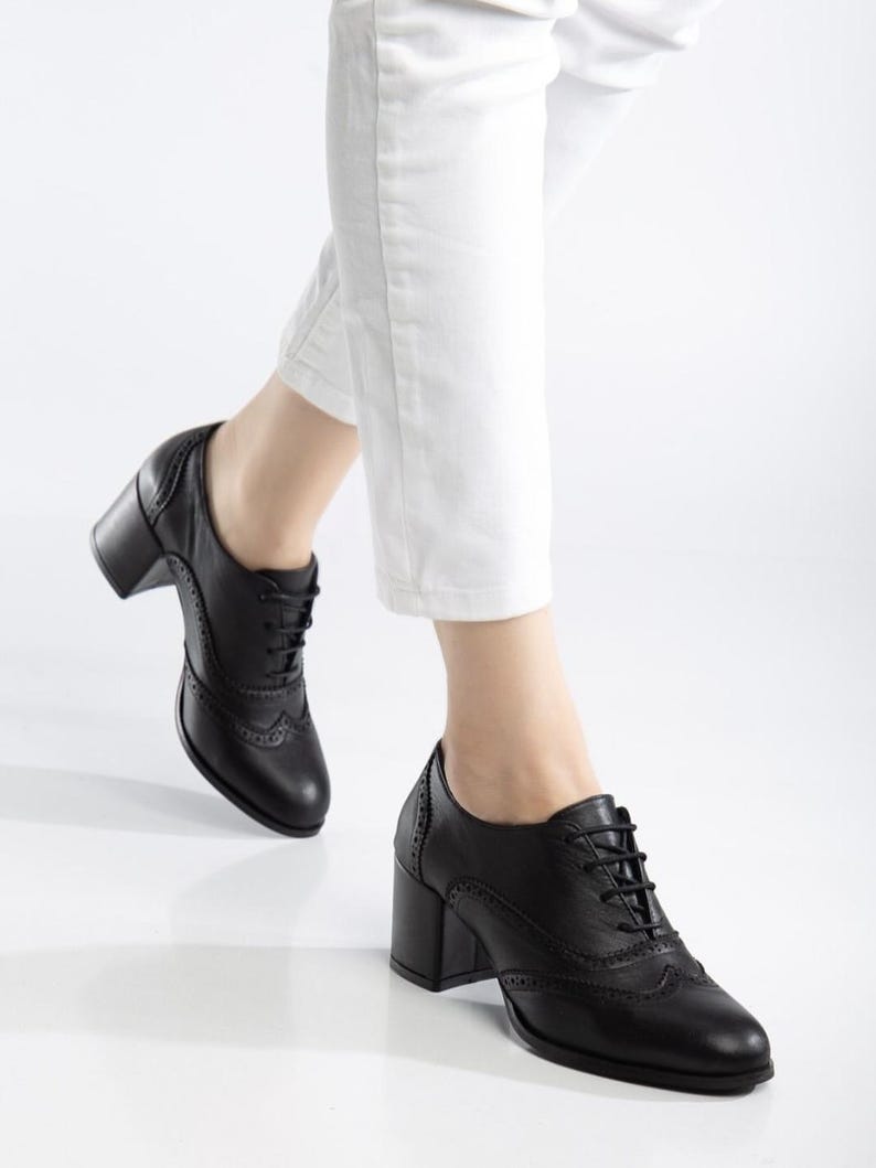 May include: Black leather oxford-style shoes with a block heel. The shoes feature a lace-up design and decorative perforations along the edges. The heel height is approximately 3 inches.