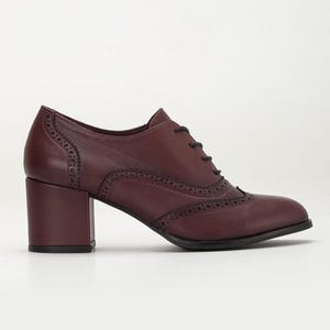 May include: Burgundy leather oxford-style shoe with a block heel. The shoe features decorative perforations along the seams and a lace-up closure. The heel measures approximately 2.5 inches.